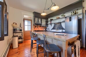 A kitchen with a wooden island, bar stools, a stainless steel refrigerator, and a hanging light fixture.