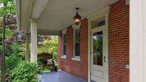 A covered porch with a brick wall, a white door, and a hanging lantern. - The Tannery  
A swanky, eclectic and fun adult retreat. (Lancaster)