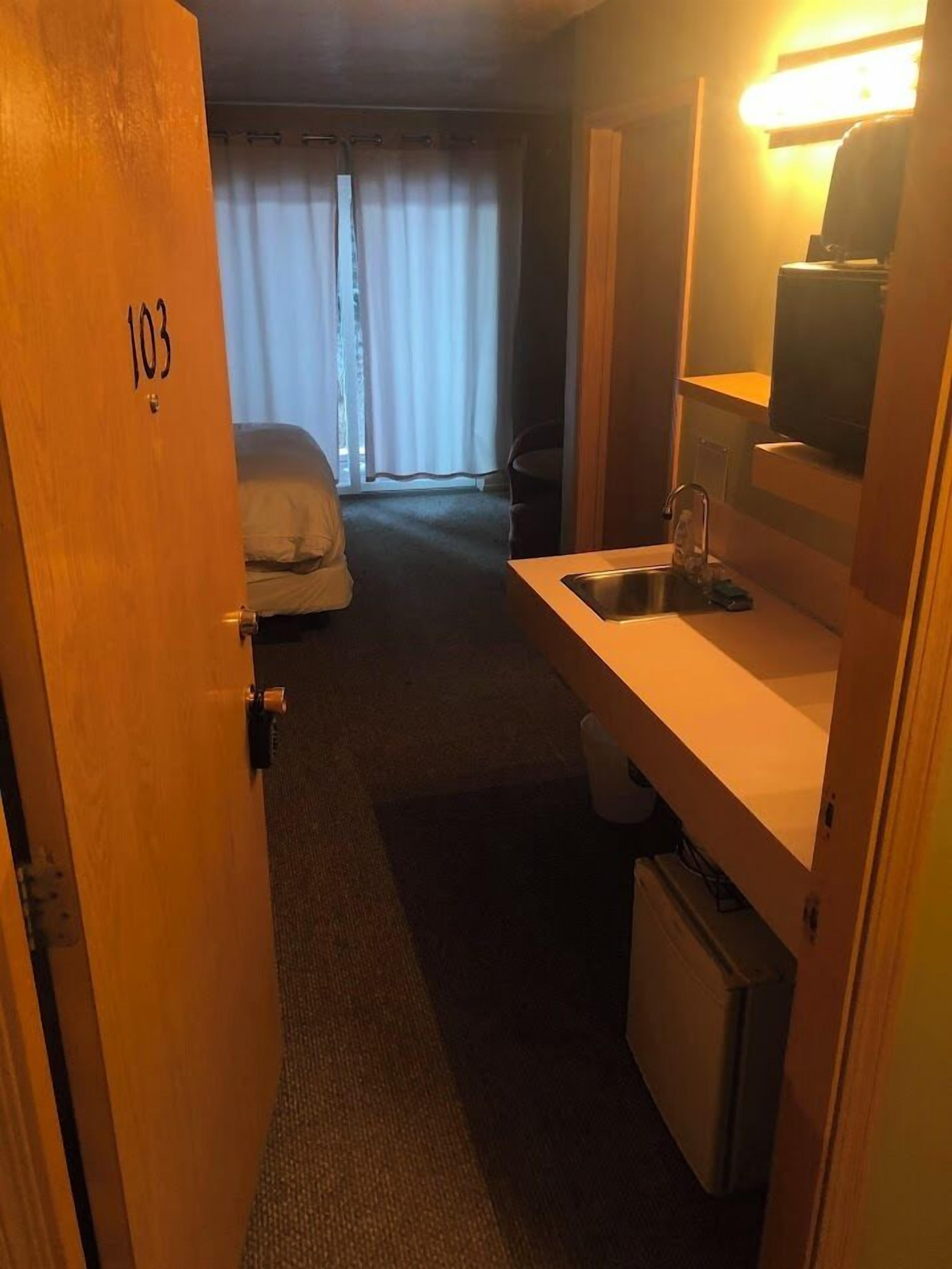 A hotel room with a bed, a small sink, and a mirror.
