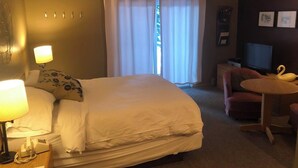 A hotel room with a bed, a desk with a lamp, a chair, a television, and a window with curtains. - Ski in/out room  with Queen and Full futon.  Sleeps 4 (Eden)