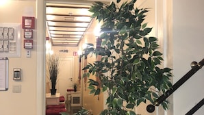 Un pasillo con una escalera, una planta en maceta y letreros de salida de emergencia.