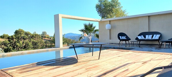 An outdoor pool area with a wooden deck, two lounge chairs, and a table.