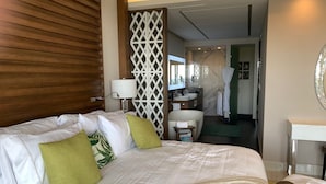 Une chambre d’hôtel avec un grand lit, une salle de bain avec un lavabo et vue sur le couloir.