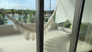 Un balcon avec un hamac, un canapé avec des coussins et une vue sur une étendue d’eau et la verdure.