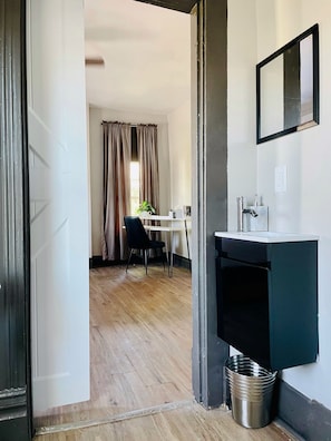 Une pièce avec un plancher en bois, un bureau avec une chaise, un lavabo et une poubelle.