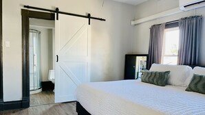 Un dormitorio con una cama grande, una puerta corrediza de estilo rústico, una ventana con cortinas y suelo de madera.