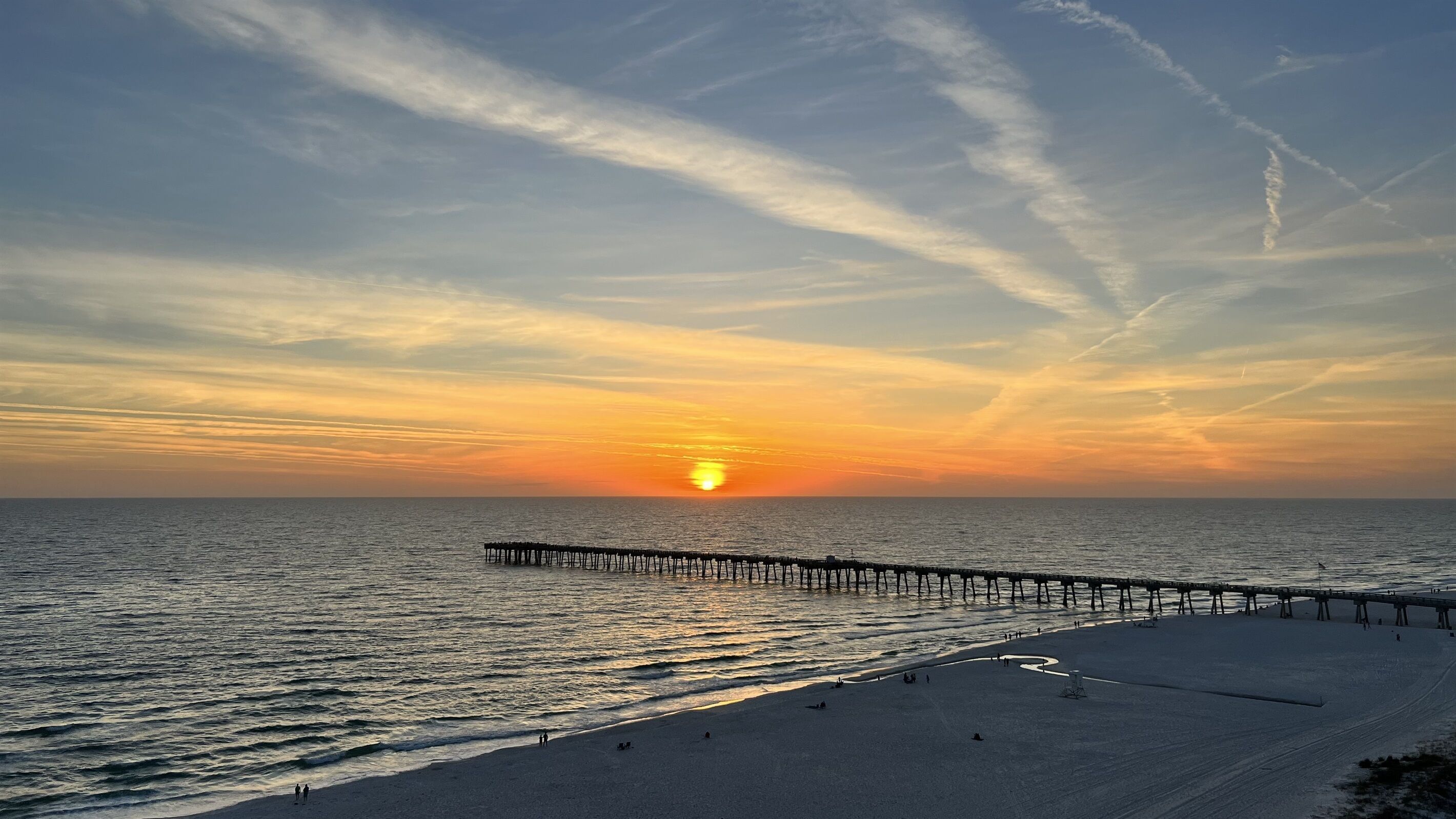 Een strand met een steiger die zich uitstrekt over de oceaan tijdens zonsondergang.