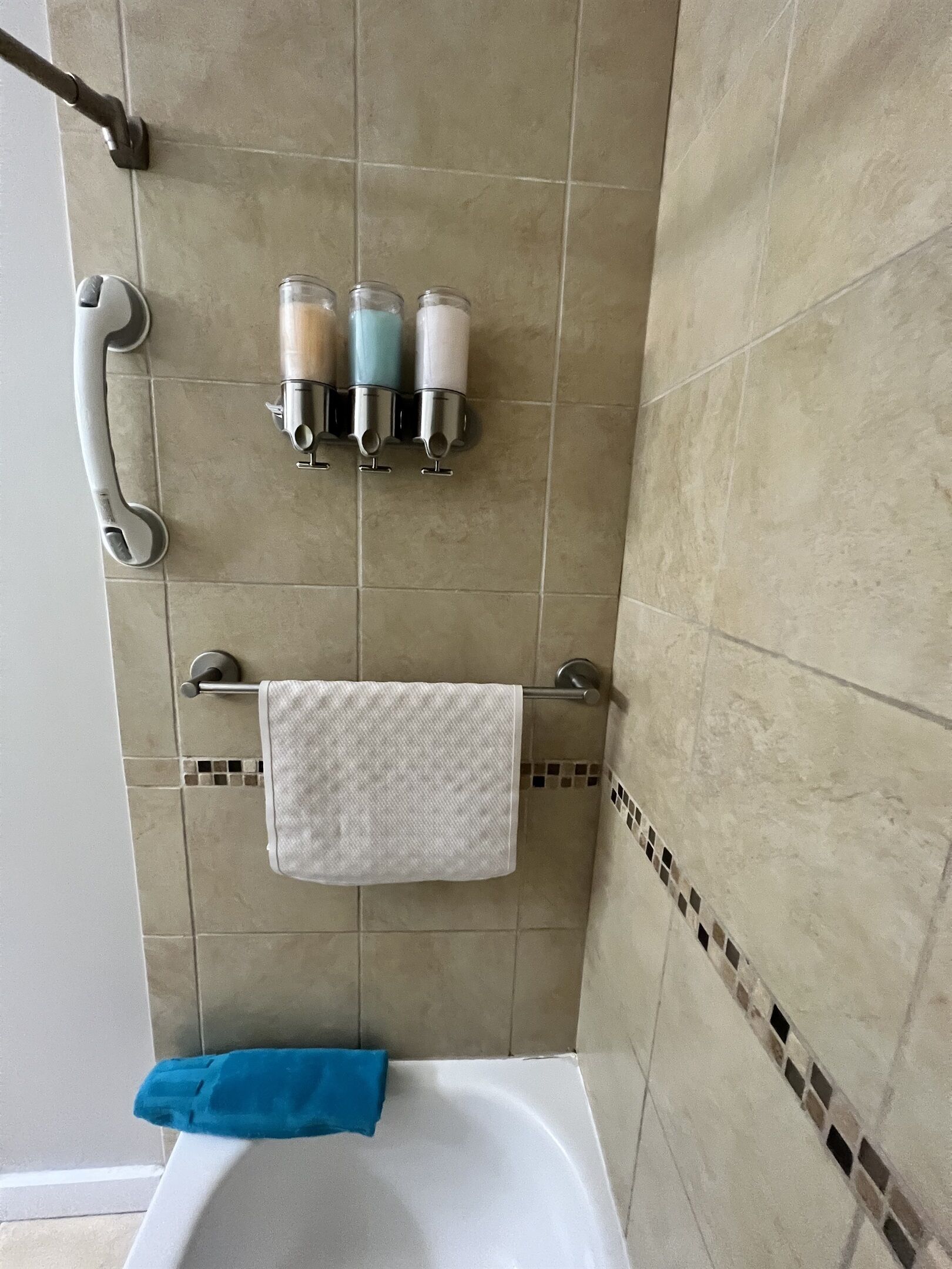 A bathroom with a bathtub, a towel rack with a white towel, and three bottles on a shelf.