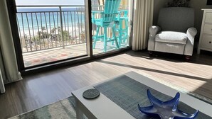 Une pièce spacieuse dotée d’une grande porte-fenêtre coulissante donnant sur un balcon avec vue sur la plage et les bâtiments.