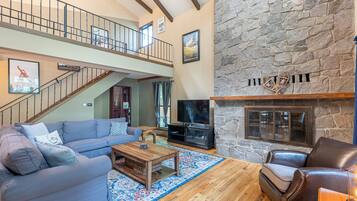 A spacious living room with a stone fireplace, a large sofa, a coffee table, and a TV.