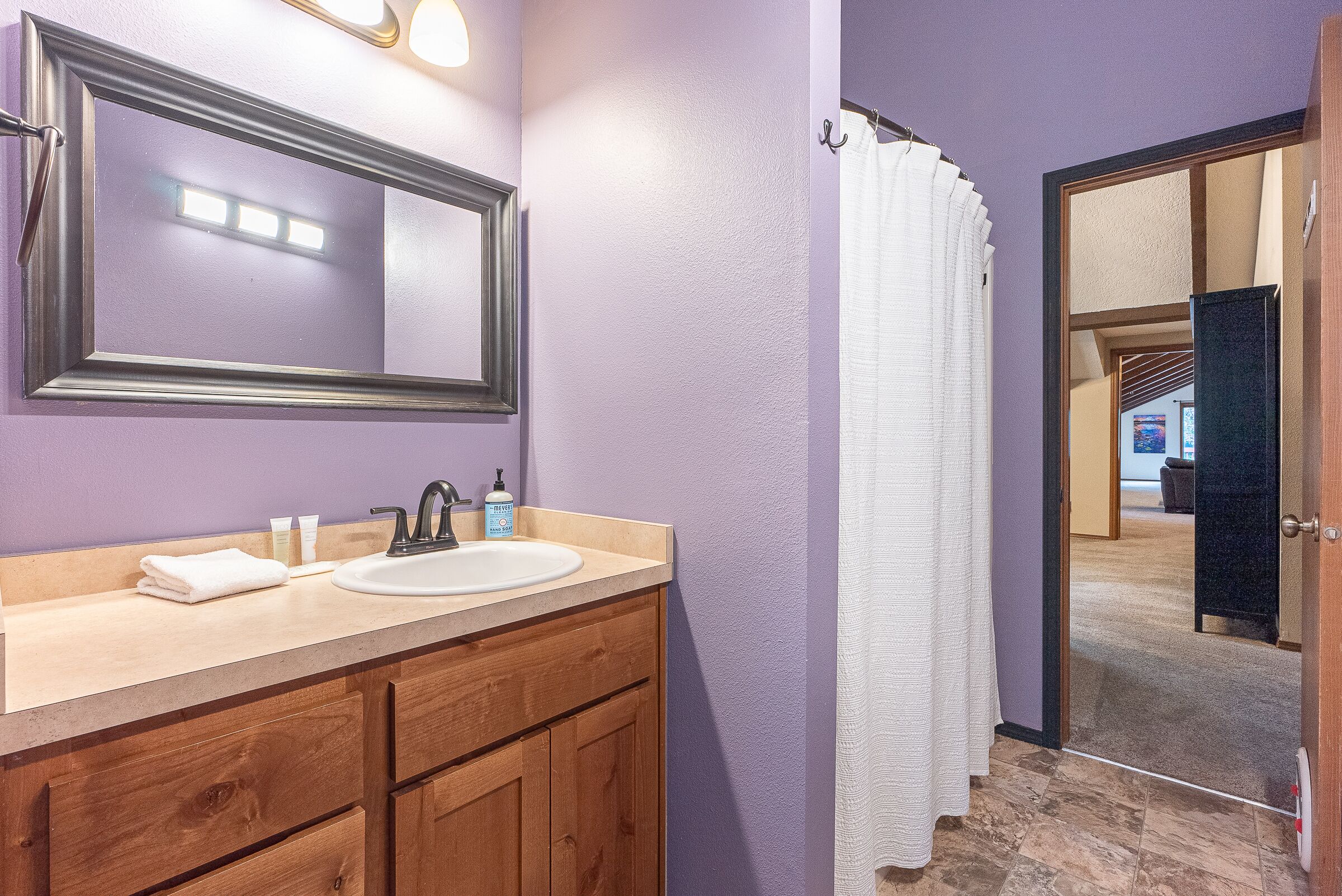 A bathroom with a wooden vanity, a large mirror, a sink, and a shower curtain.