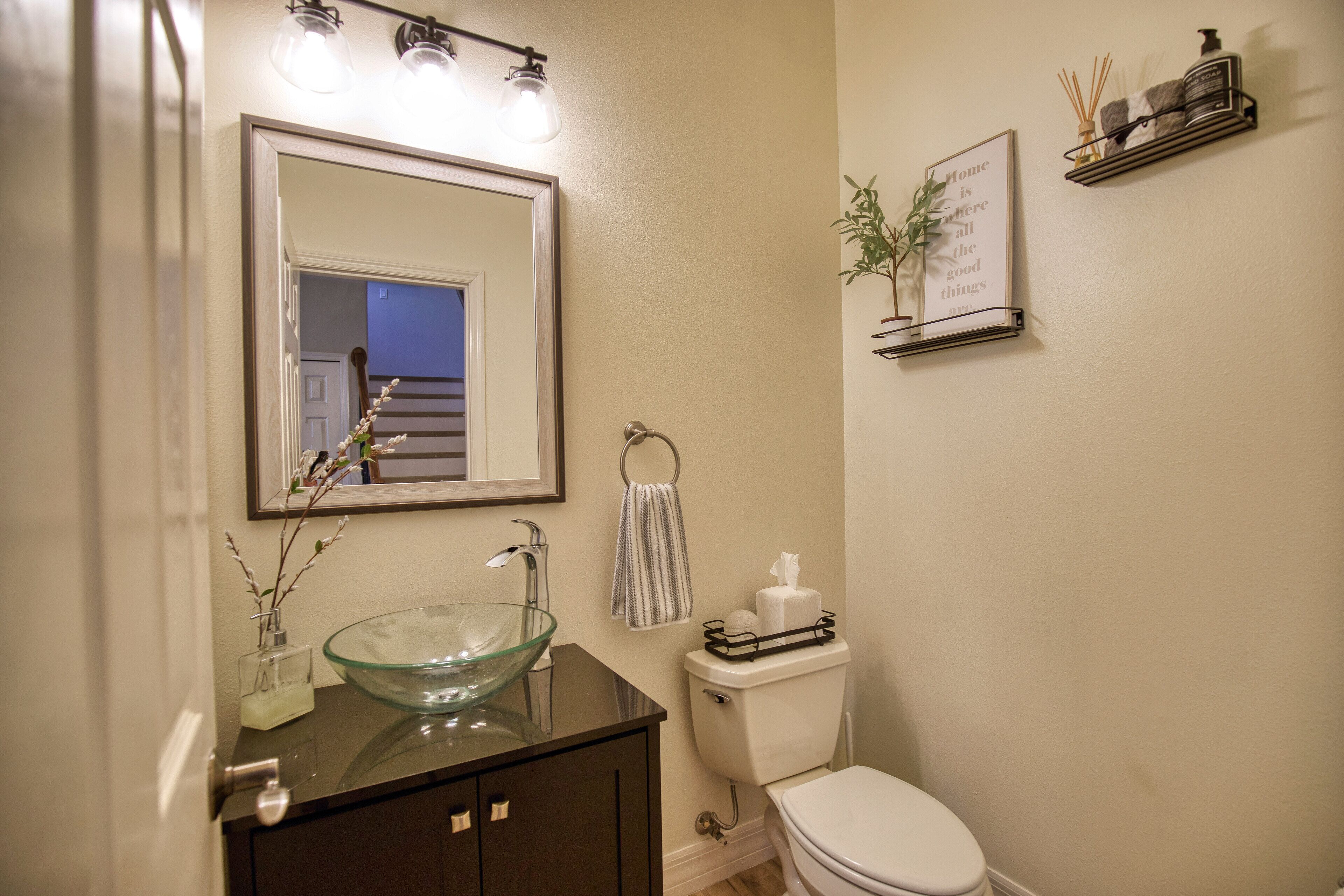 Une salle de bain avec un lavabo en forme de bol en verre, des meubles sombres, des toilettes blanches et un miroir avec éclairage intégré.