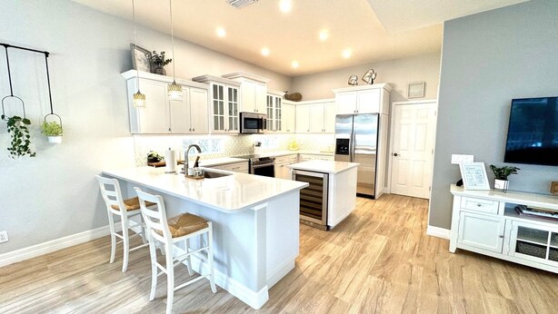 A modern kitchen with white cabinetry, a central island with bar stools, a microwave, oven, and refrigerator. - 4 Bedroom Pool Home Siesta Key (Siesta Key)