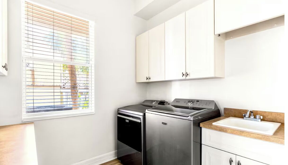 A compact kitchen with a built-in washer and dryer, a sink, and white cabinetry.