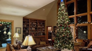 A cozy living room with a large Christmas tree, a fireplace, and a bookshelf filled with books and decorations.