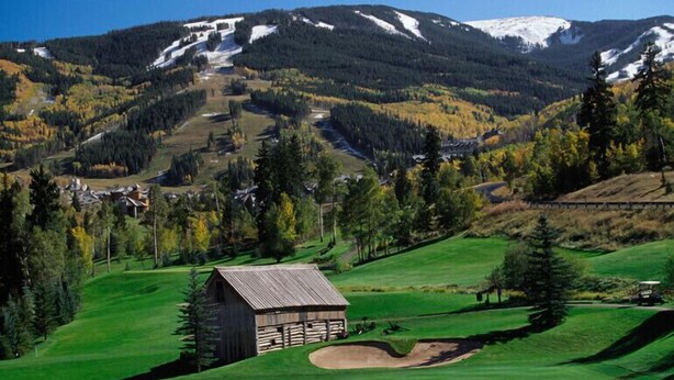 A golf course with a wooden cabin, a mountain backdrop, and a clear sky.
