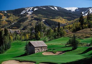 A golf course with a wooden cabin, a mountain backdrop, and a clear sky.