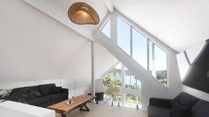 Amplia sala de estar con un ventanal grande, una mesa de centro de madera, un sofá negro y una lámpara colgante.
