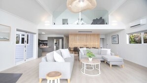 Una sala de estar moderna con un sofá gris, una mesa de centro redonda y un comedor con una pared de madera y una lámpara colgante.