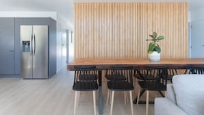 Una cocina moderna con una mesa de comedor de madera y sillas negras, un refrigerador de acero inoxidable y un panel de pared de madera vertical.