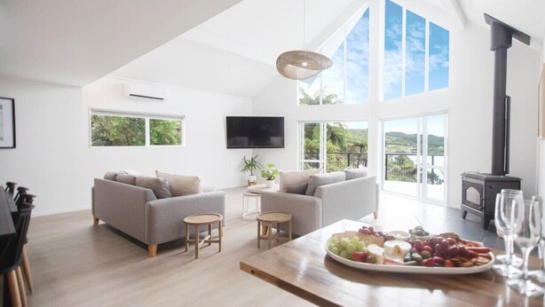 Amplia sala de estar con techos altos, ventanas grandes, chimenea y un comedor con una bandeja de frutas.