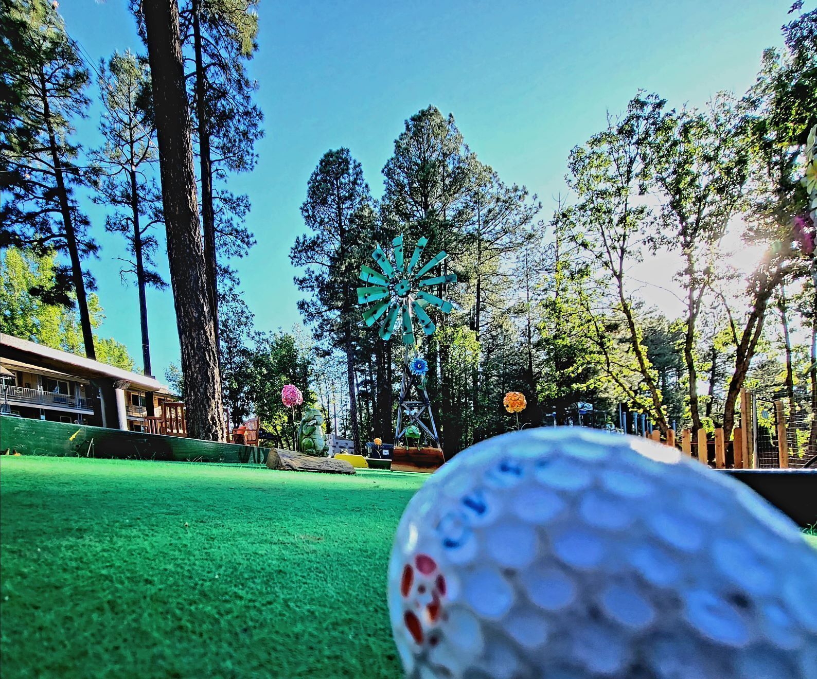 Ein Golfplatz mit Windmühle, Bäumen und einem Gebäude im Hintergrund.
