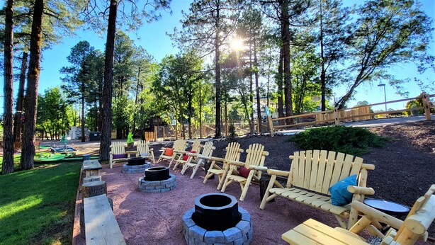 A forested outdoor area with wooden Adirondack chairs and fire pits. - The Nook Pinetop (Pinetop)