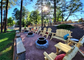 A forested outdoor area with wooden Adirondack chairs and fire pits. - The Nook Pinetop (Pinetop)