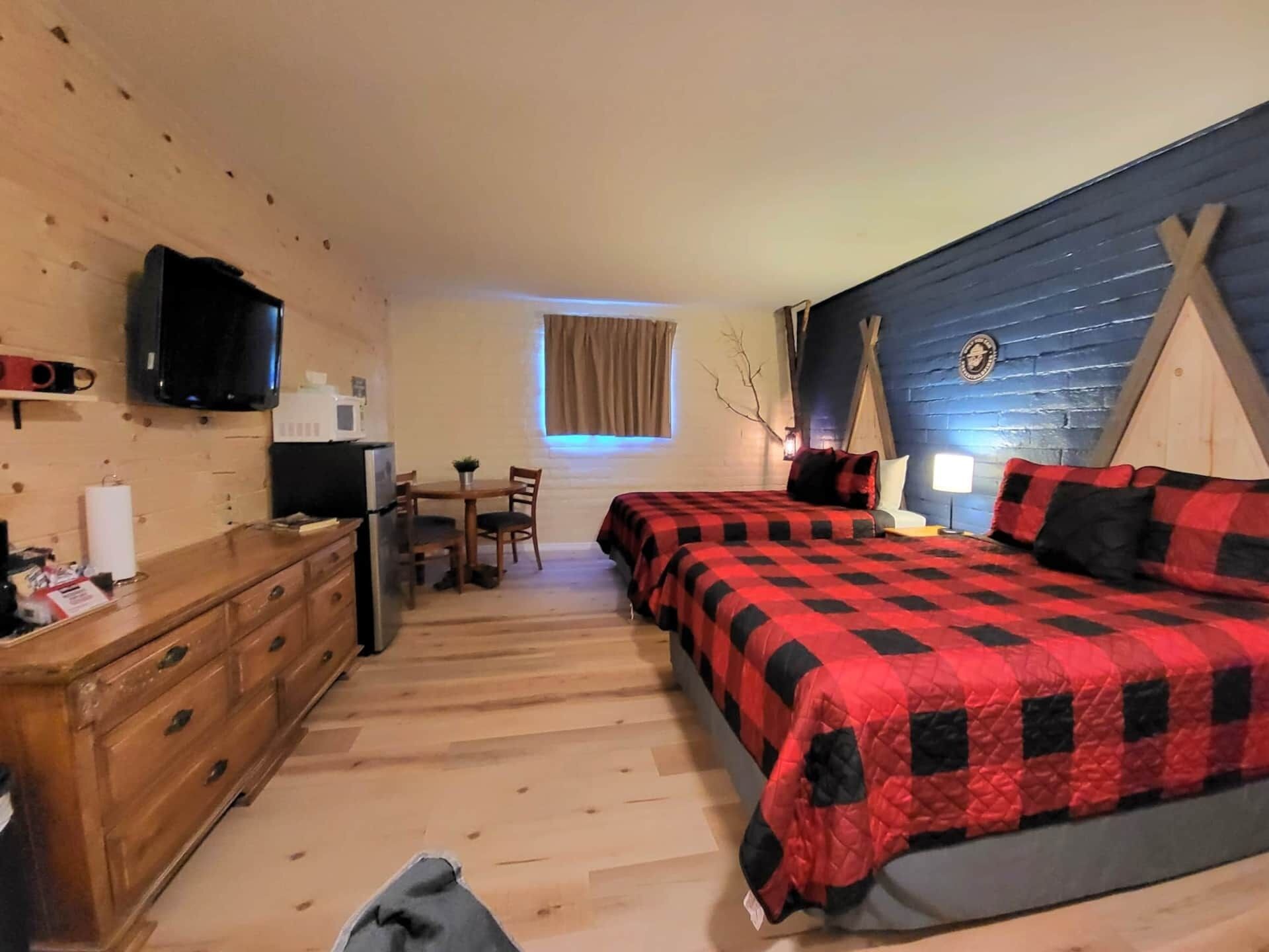 A compact room with a bed, a desk, a chair, a dresser, a television, and a window with curtains.