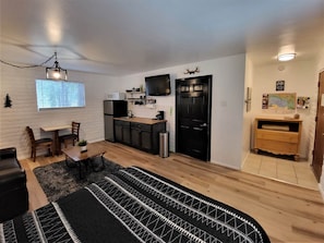 Un espacio habitable compacto con kitchenette, zona de comedor, una puerta negra y un pequeño armario de madera.
