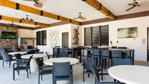 A spacious outdoor dining area with multiple round tables and chairs, ceiling fans, and a stone fireplace. - Beautiful home-private spa/pool 5BD 5.5 BA (Davenport)