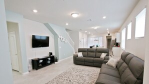 A spacious living room with a large flat-screen TV, two sofas, a patterned rug, and a staircase leading to another level. - Beautiful home-private spa/pool 5BD 5.5 BA (Davenport)