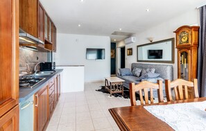Une cuisine moderne avec des meubles en bois, une cuisinière et un four à micro-ondes. On y trouve un coin repas avec une table et des chaises, ainsi qu’un salon avec un canapé et un téléviseur.