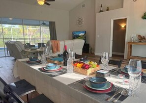 Un coin repas avec une table dressée pour quatre personnes, un canapé en arrière-plan et une grande fenêtre donnant sur un paysage verdoyant.