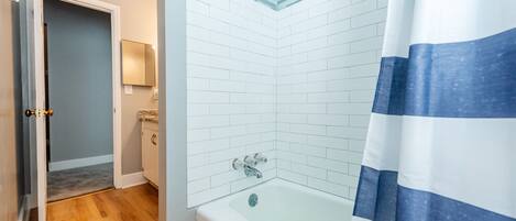 A bathroom with a white tiled shower, a bathtub, and a striped shower curtain.