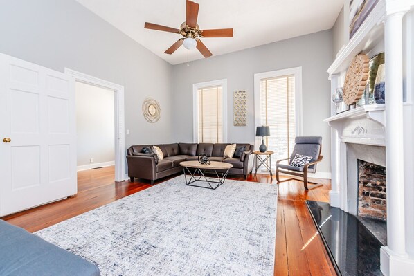 A living room with a sectional sofa, a coffee table, a fireplace, and a ceiling fan.