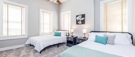 A bedroom with two beds, a ceiling fan, and large windows with blinds.