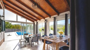 Un'ampia stanza con soffitto in legno, grandi finestre, una piscina e un tavolo con pedine per gli scacchi.