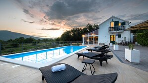 Una piscina con lettini e una casa moderna con un balcone.