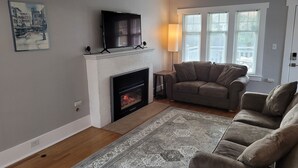Una sala de estar con chimenea, un sofá, un televisor y una ventana con persianas.
