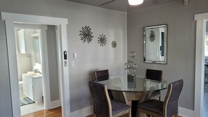 Un comedor con mesa de vidrio y sillas de metal, ventilador de techo y decoración mural.