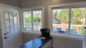 Una cocina con encimera oscura, cafetera y dos ventanas que dan a un jardín trasero.