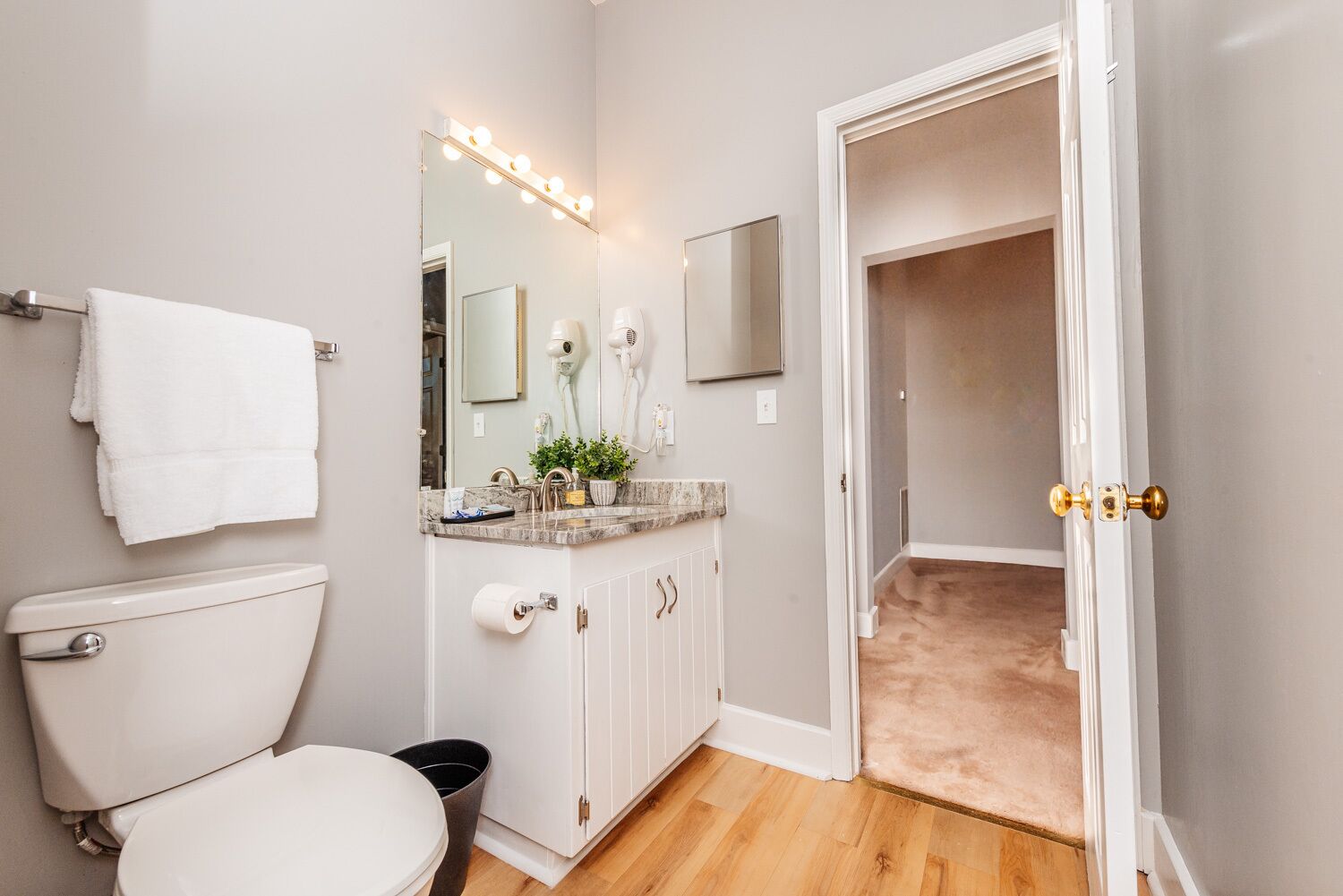 A bathroom with a toilet, sink, vanity, and a mirror with lights.
