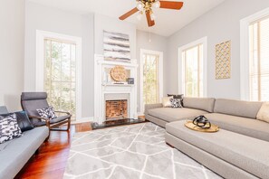 A living room with a fireplace, a ceiling fan, and a large window.