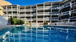Um hotel com vários andares, piscina, varandas e um céu azul límpido.