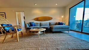 Uma sala de estar moderna com uma janela grande, uma mesa de centro redonda, um sofá e uma cadeira de vime.
