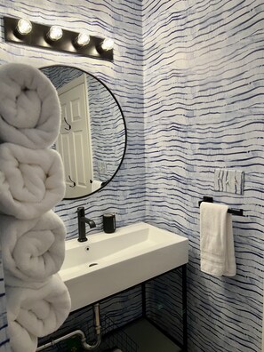 Een badkamer met een witte wastafel, een ronde spiegel met verlichting erboven, een handdoekhouder en een muren met een patroon.