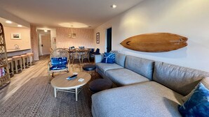 Uma sala de estar moderna com um sofá cinzento, uma mesa de centro redonda e um espaço de jantar com mesa e cadeiras de madeira.