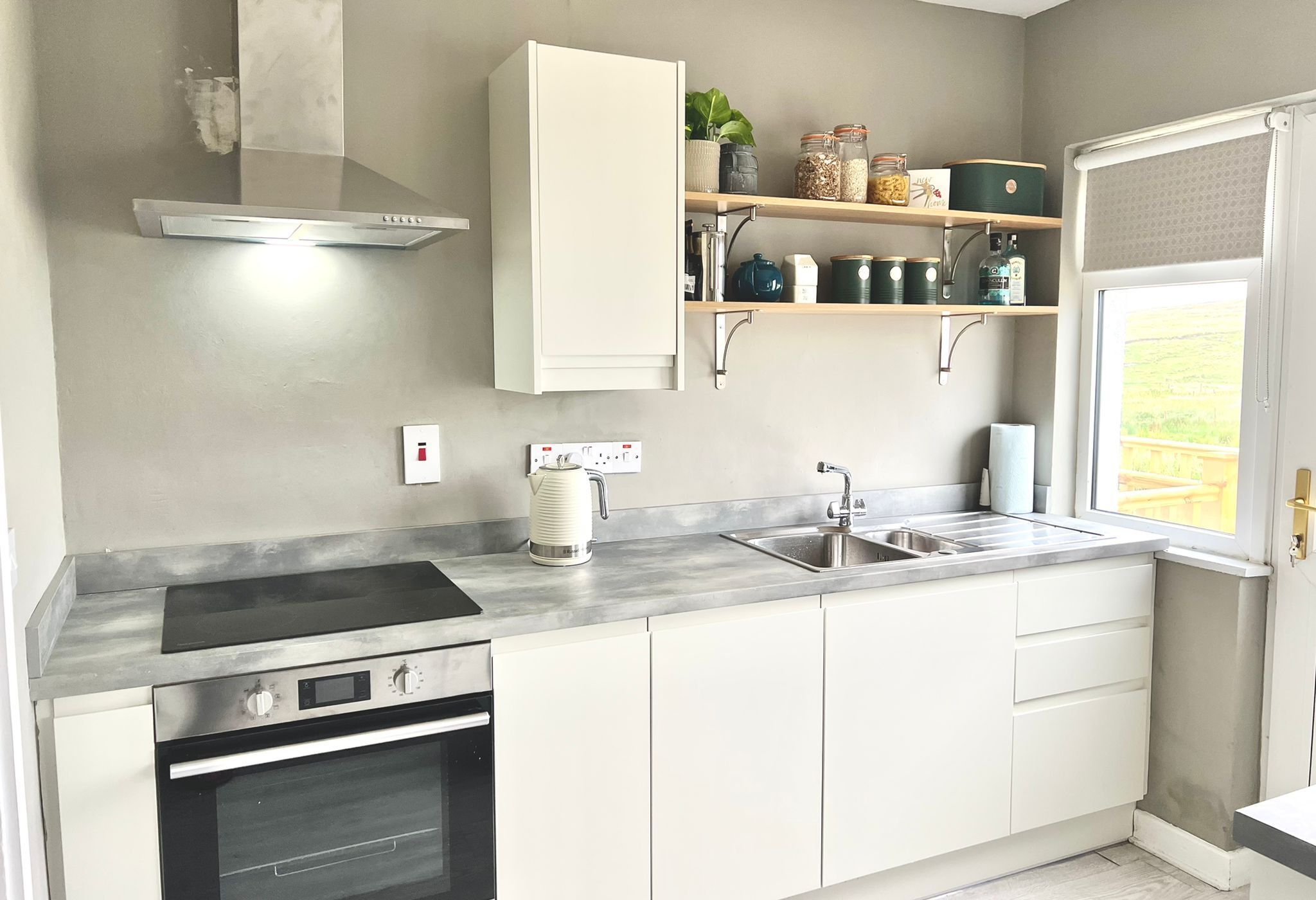 A modern kitchen with a built-in oven, stainless steel range hood, and a window with a view of the outdoors.