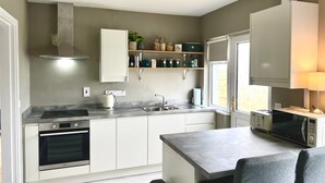 Una cocina moderna con horno empotrado, microondas y un amplio ventanal que proporciona luz natural.